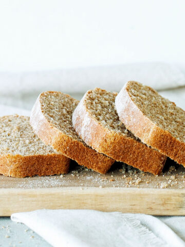 Several leaning whole wheat bread slices on a wooden board. White background.