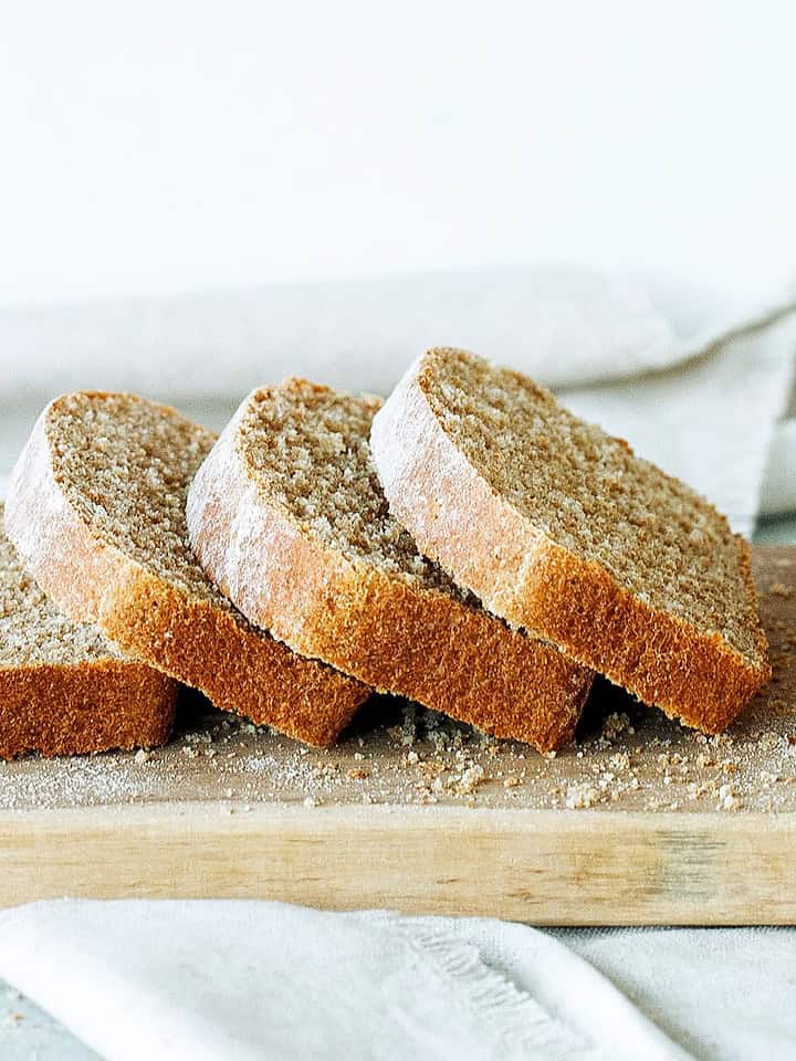 Several leaning whole wheat bread slices on a wooden board. White background.