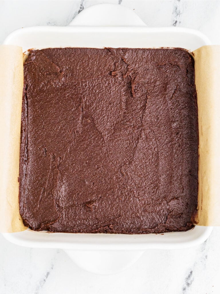Brownie layer in a parchment-lined white dish.