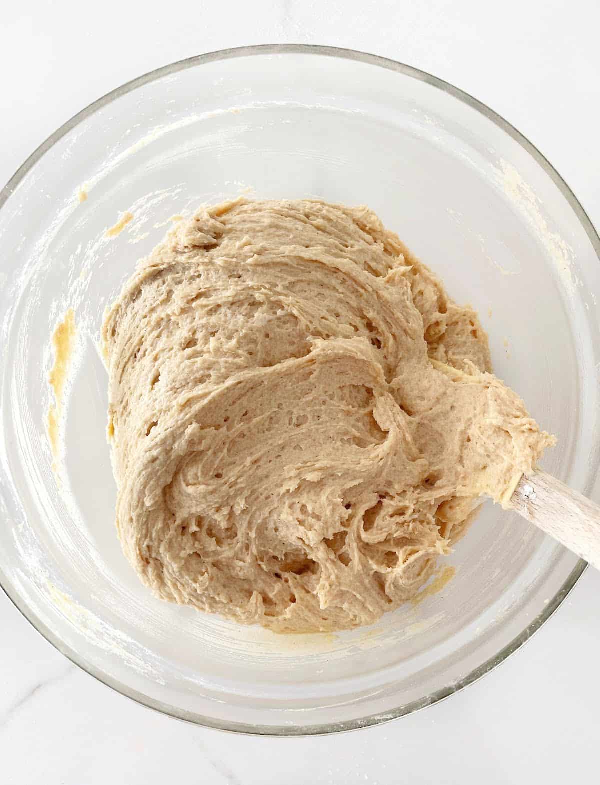 Cinnamon cake batter in a glass bowl with a spatula on a white surface.