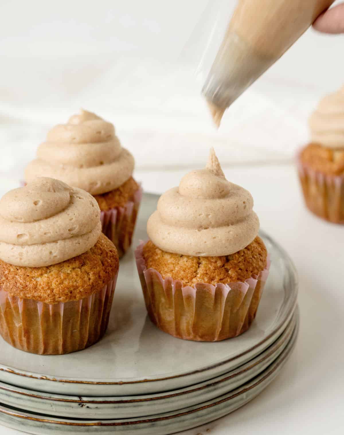 Frosting piped on paper-lined cupcakes on a gray plate. White background.