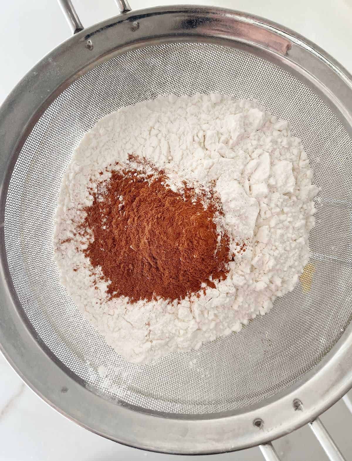 Flour mixture and cinnamon being sifted. Close up top view image.