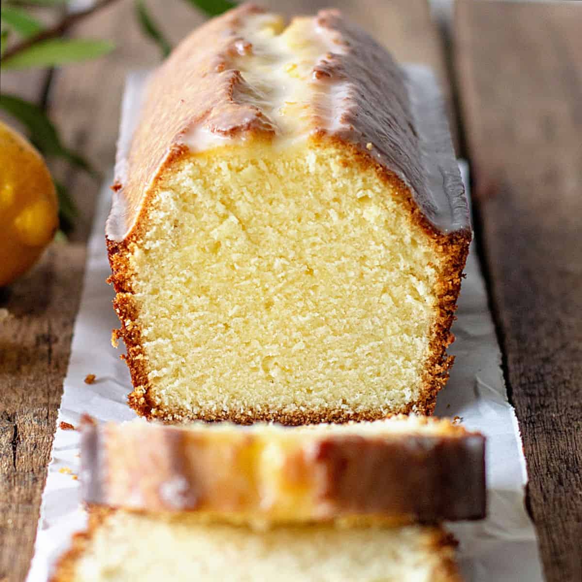 Cut glazed lemon loaf cake on a white paper on a wooden surface.