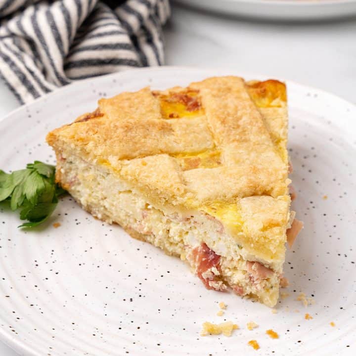 A single slice of savory ricotta lattice pie on a white plate. Striped cloth and rest of pie in the background.