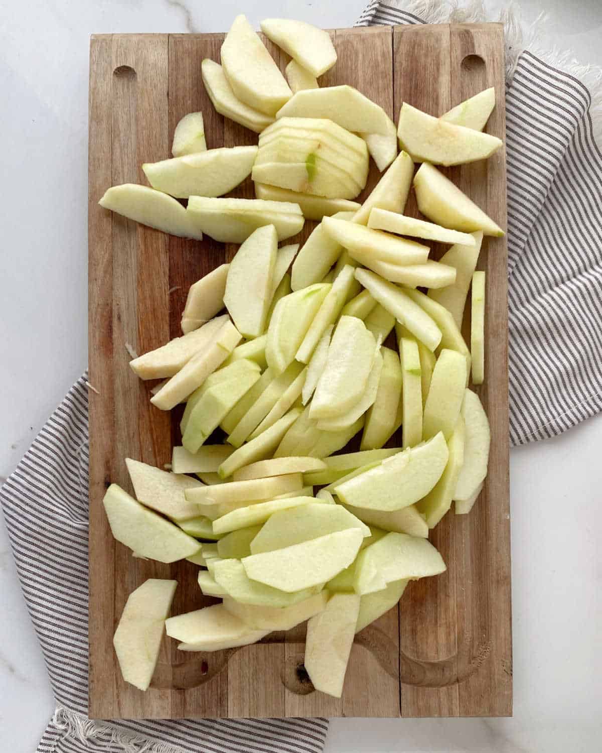 Apple slices on a wooden board over a striped cloth on a white marble surface. View from above.