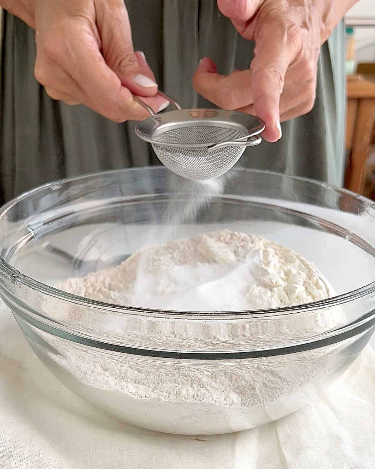 Sifting baking soda over whole wheat and white flours in a glass bowl. Green dress background.