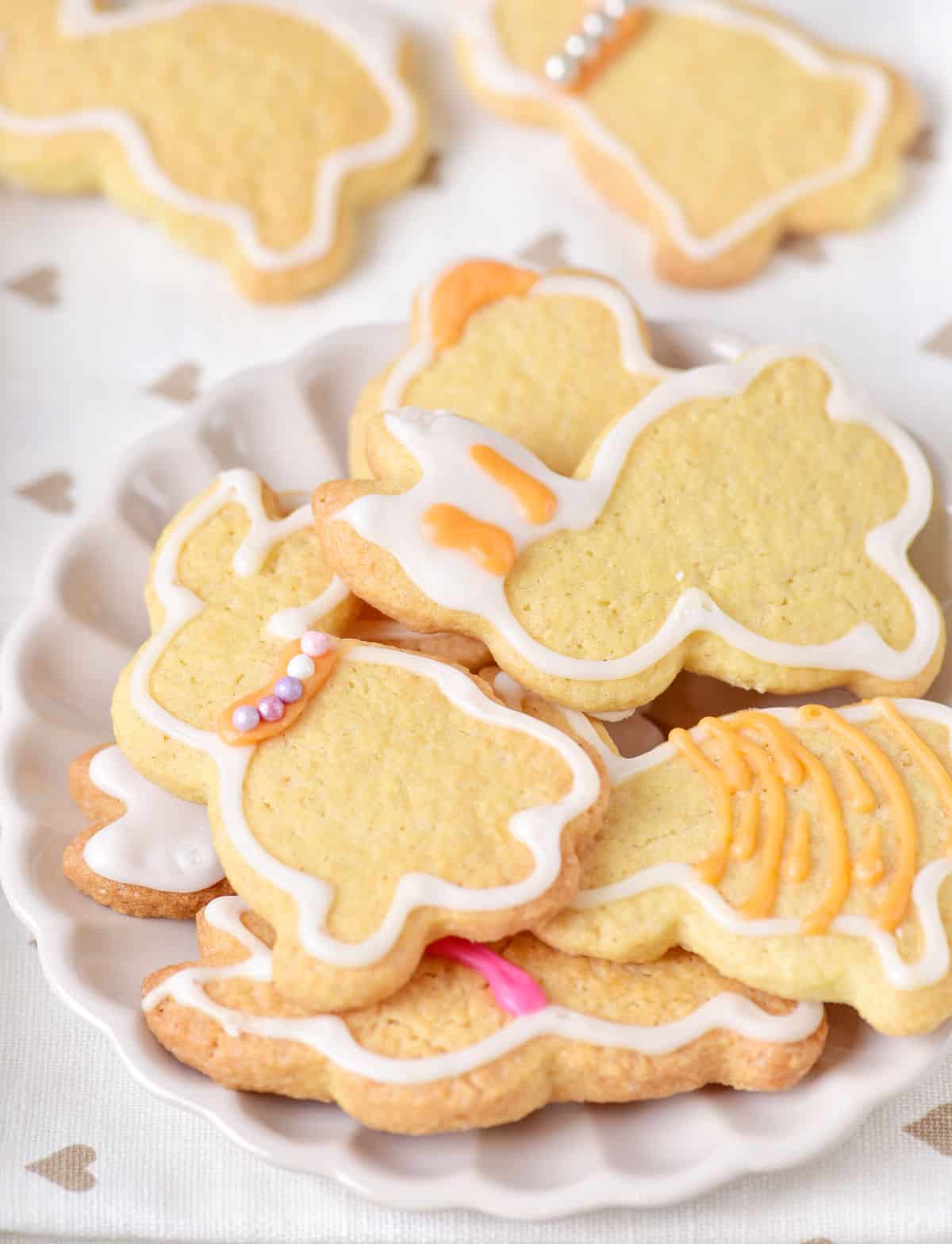 White plate with a pile of white and orange glazed bunny cookies. White surface with grey hearts.