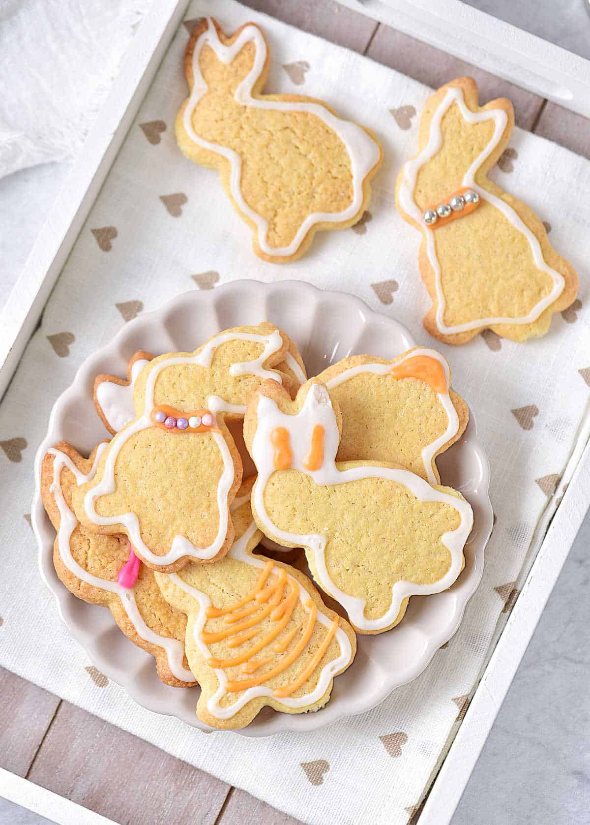 Top view of white and beige tray with white plate containing a pile of orange and white glazed bunny sugar cookies. 