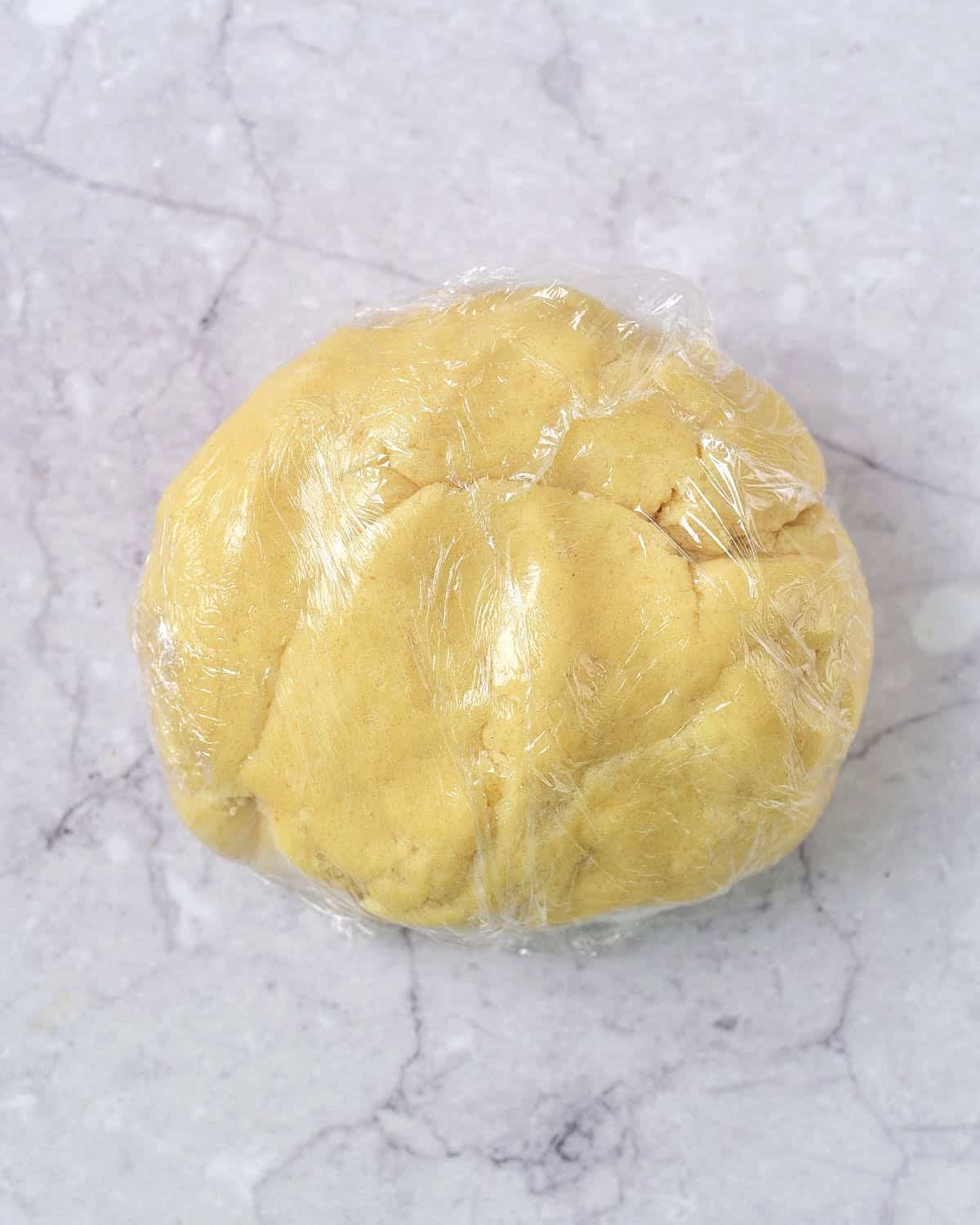 Disc of sugar cookie dough wrapped in plastic on a grey marble surface.