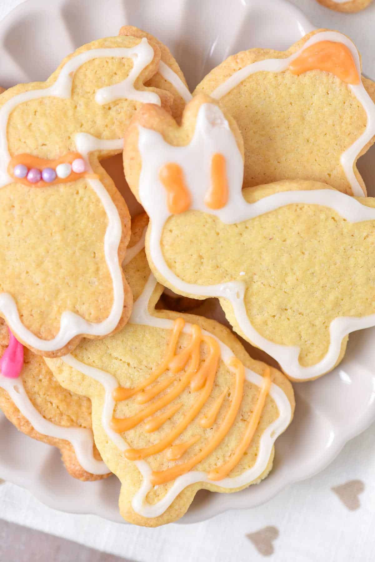 Close up of several orange and white glazed bunny sugar cookies piled on a white plate.