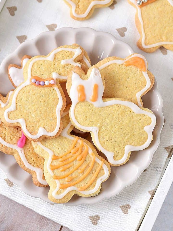Overview of white plate with a pile of iced bunny sugar cookies on a white tray with beige hearts.