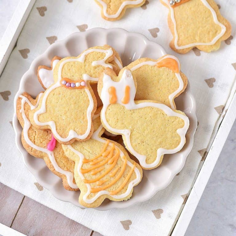 Overview of white plate with a pile of iced bunny sugar cookies on a white tray with beige hearts.