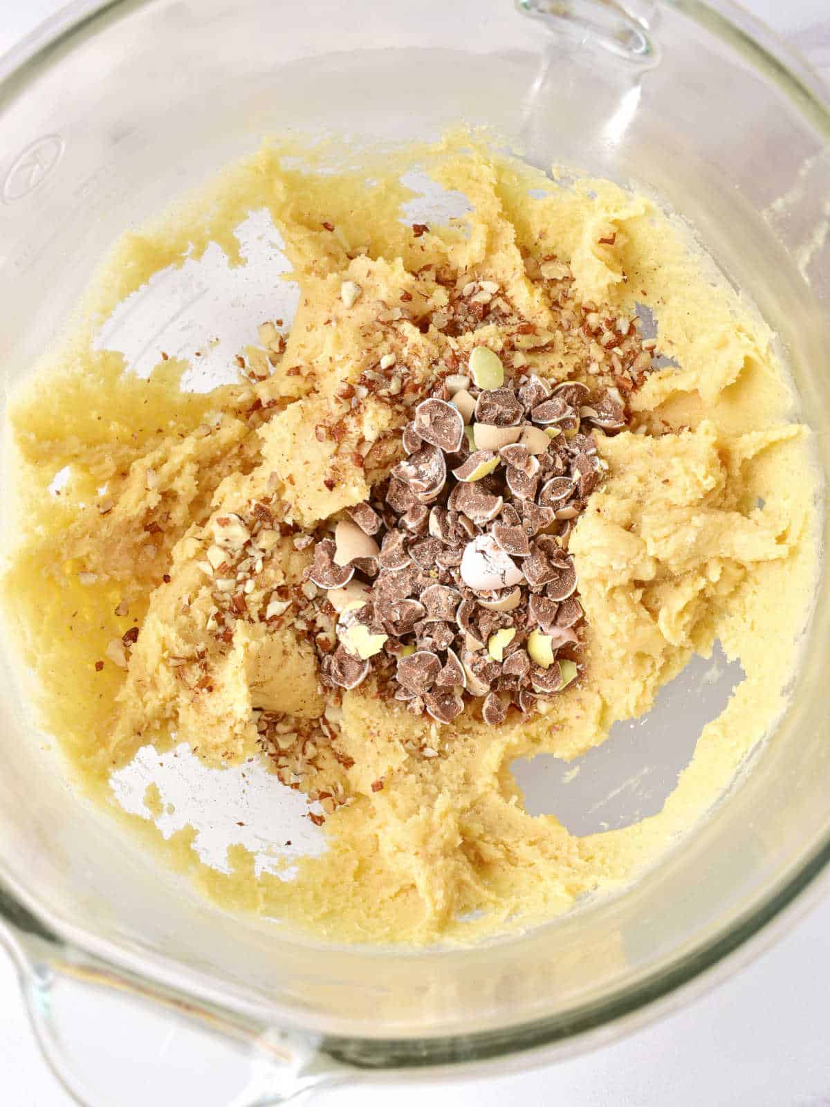 Vanilla cookie batter with chopped chocolate mini eggs in a glass mixer bowl. 