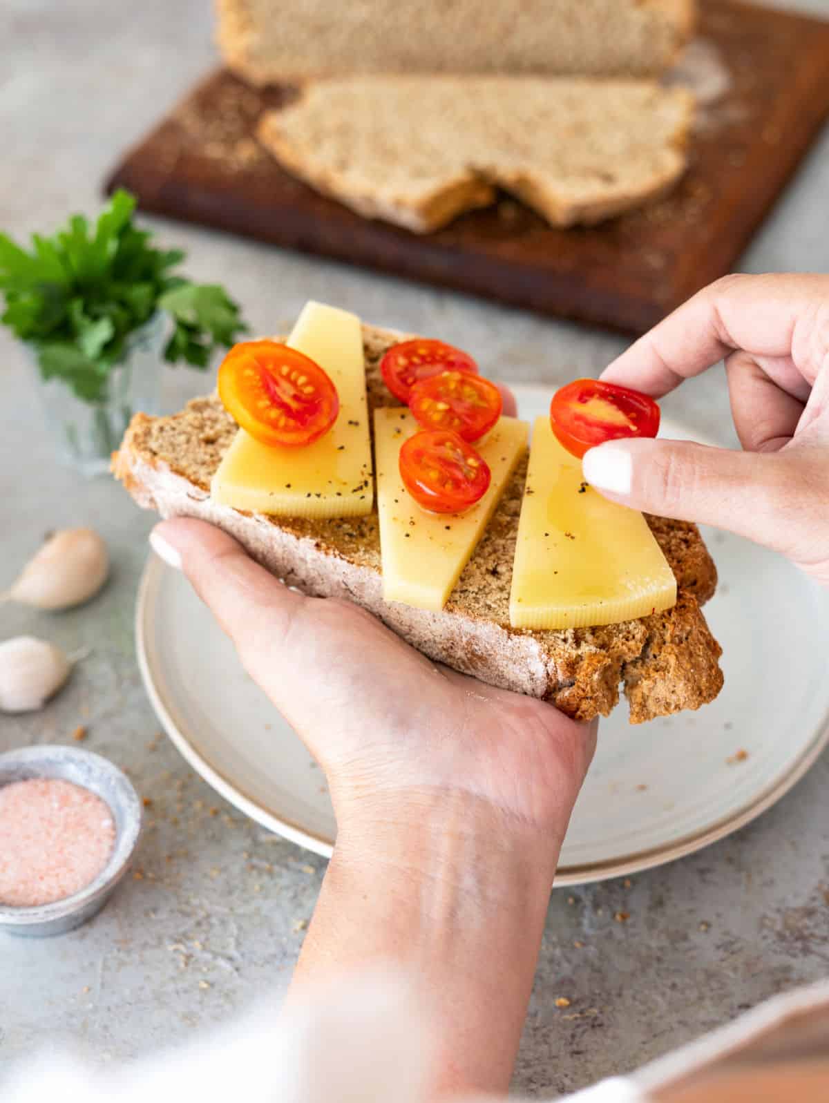 Adding cherry tomato halves to a slice of whole wheat bread with cheese being held.
