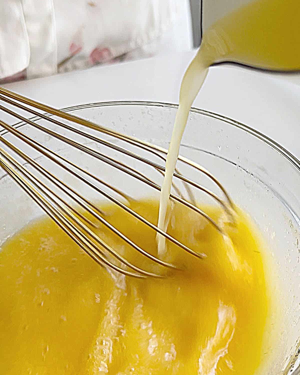 Whisking melted butter and lemon juice into beaten eggs in a glass bowl.