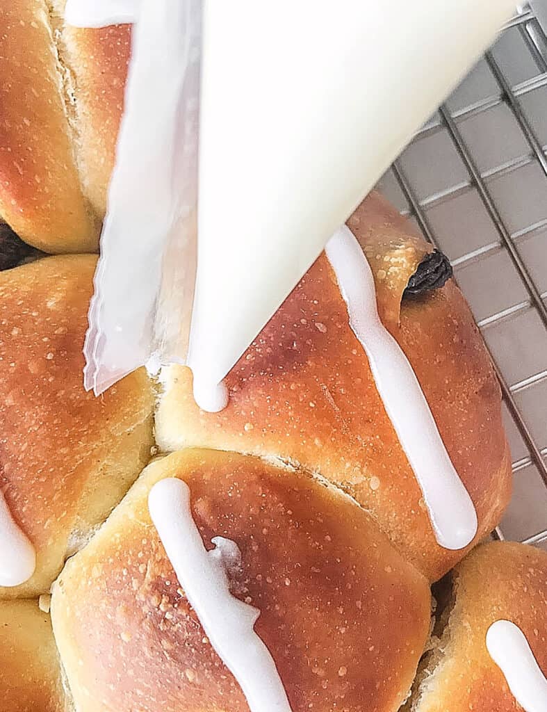 Piping white lines on baked small raisin rolls.