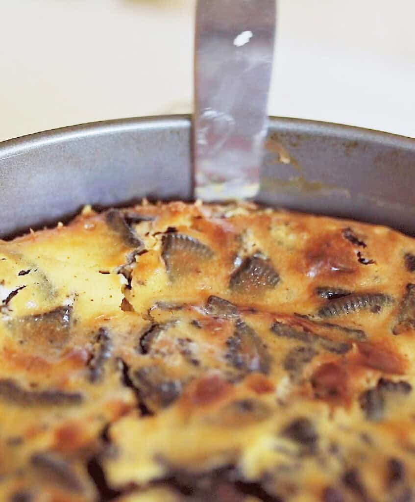 Running a knife around the edges of an Oreo cheesecake in a round pan.