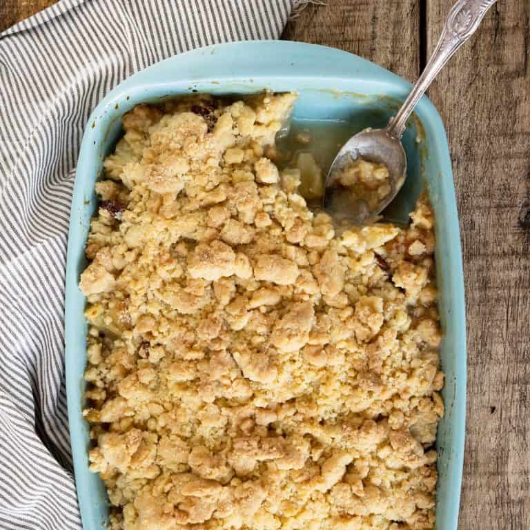 Eaten pineapple dump cake in a light blue baking dish with a spoon inside. Wooden surface with a striped cloth.