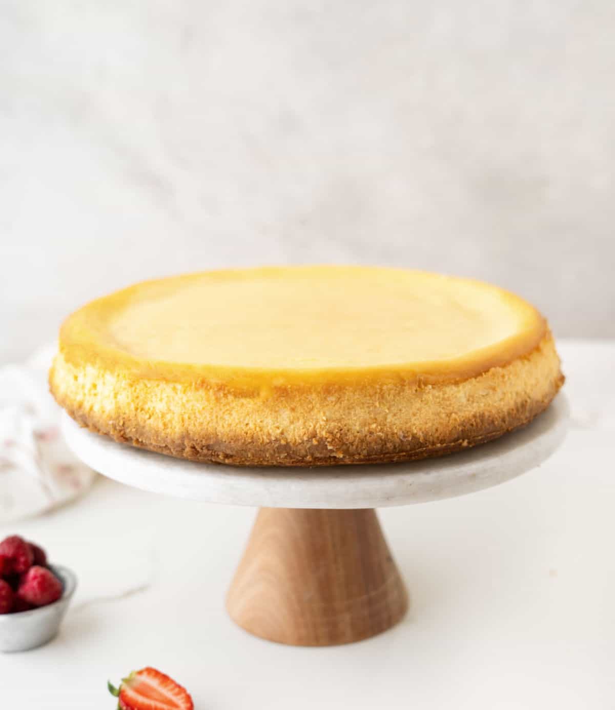 Plain ricotta cheesecake on a marble and wood cake stand. Grey background and white marble surface. 