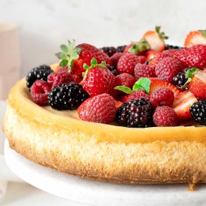 Close up of fresh berry topped ricotta cheesecake on a white marble plate with a light grey background.