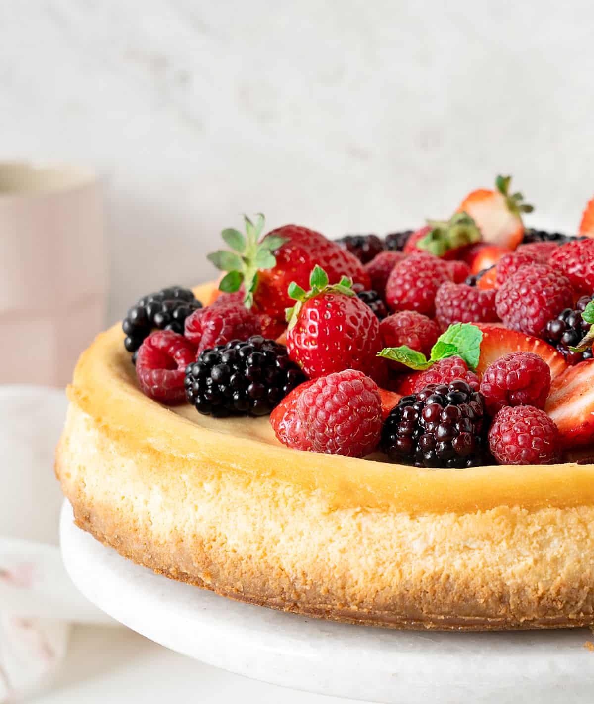 Partial view of ricotta cheesecake topped with fresh berries on a white marble plate. Light grey background. 