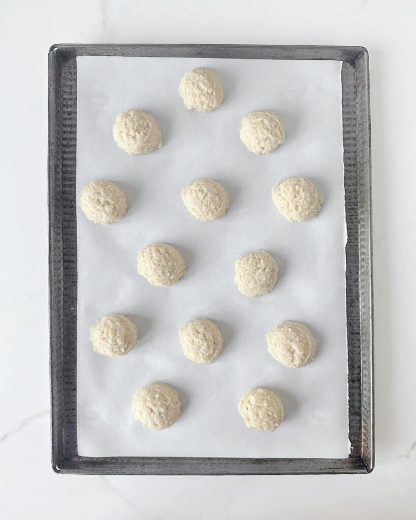 Cookie sheet with unbaked almond macaroons on parchment paper. White marble surface.