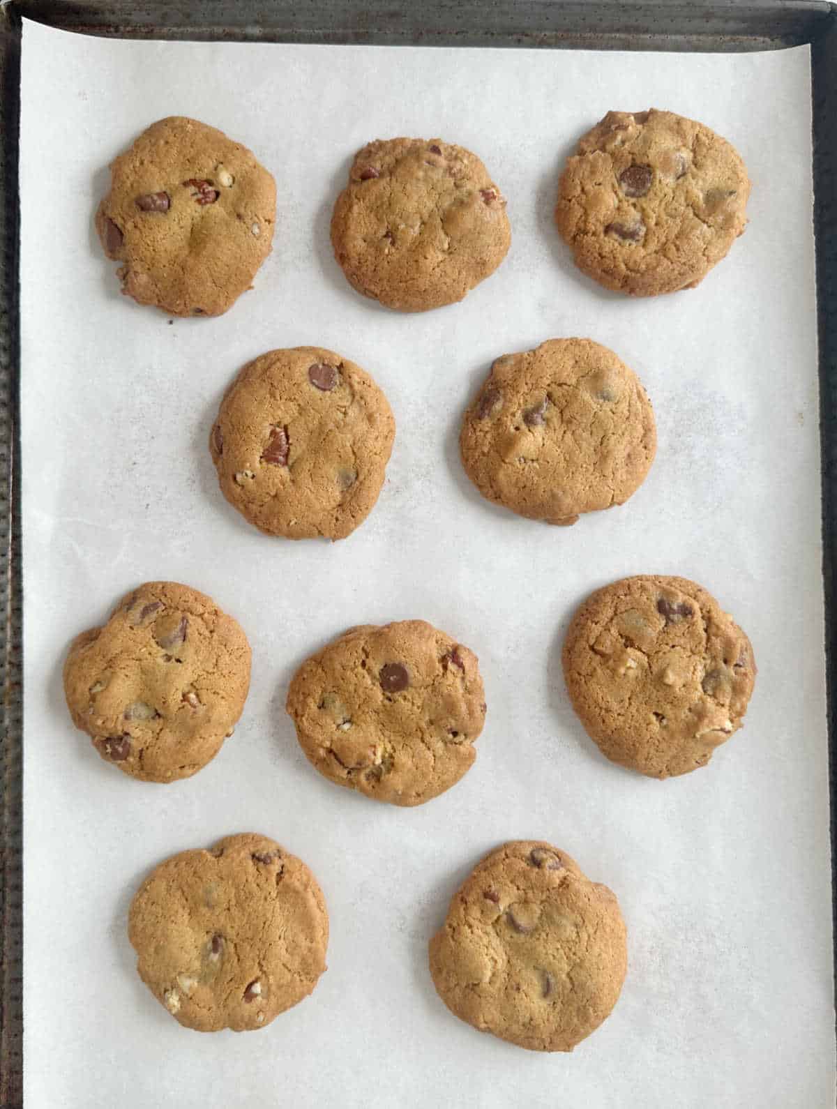 Baked chocolate chip pecan cookies on parchment paper.