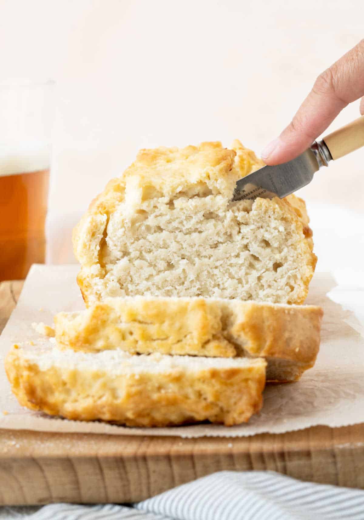 Front view of beer bread being sliced on a wooden board with parchment paper. 