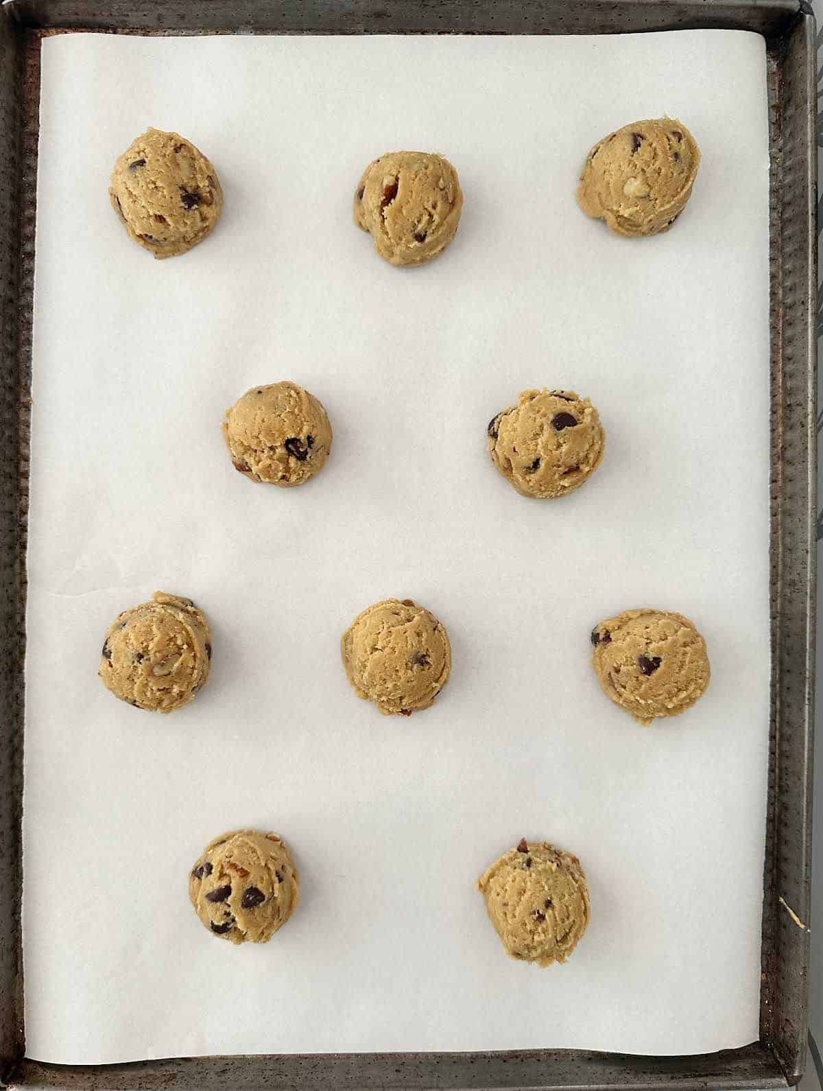 Parchment paper lined cookie sheet with chocolate chip pecan cookie scoops.