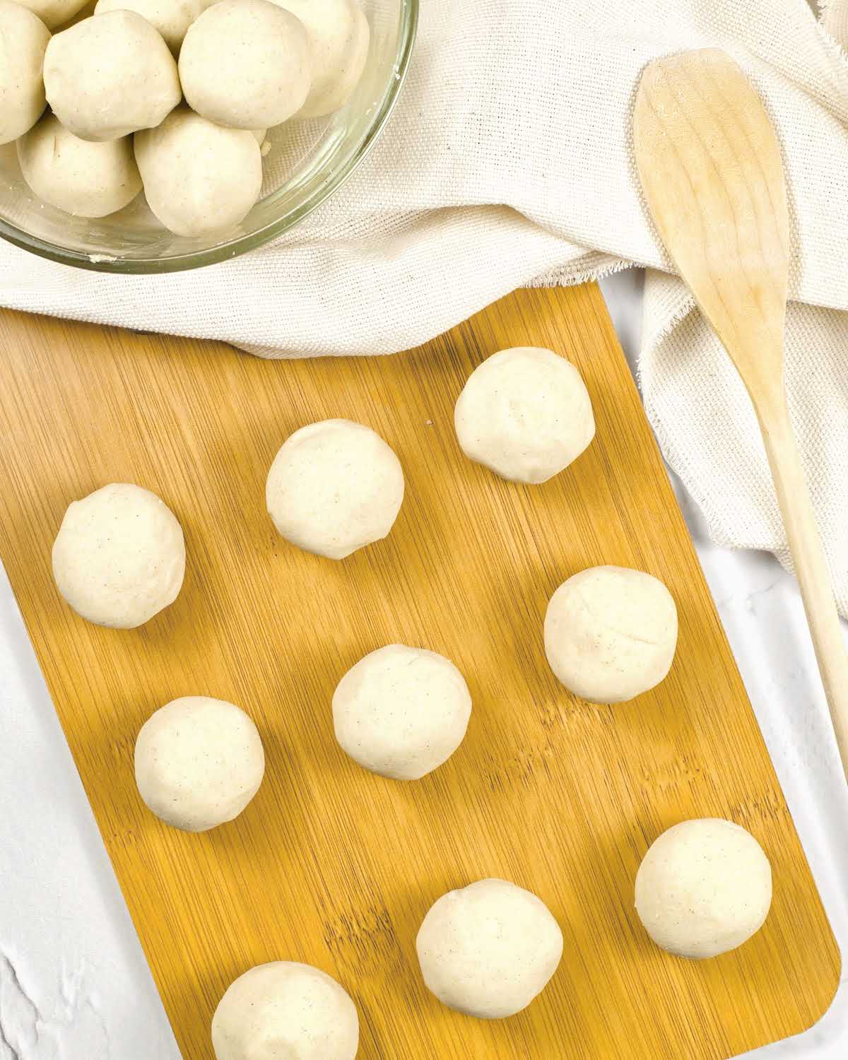 Wooden board with masa harina dough balls. White cloth and wooden spoon.