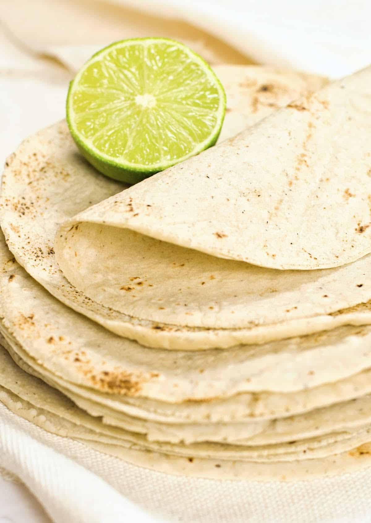 Stack of corn tortillas with half a lime and top one folded. White background. 