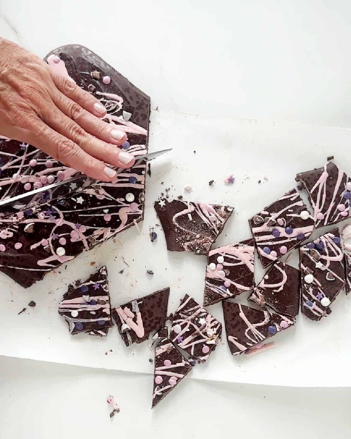 Cutting dark chocolate and pink bark with a kitchen knife on a piece of parchment paper.