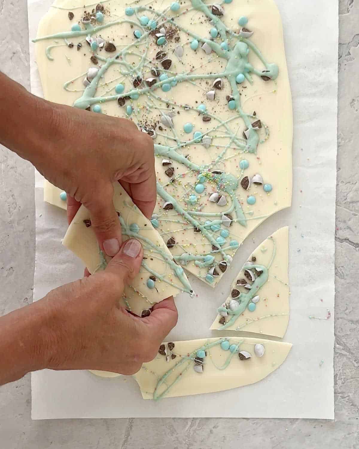 Breaking pieces of white and pastel green chocolate bark on parchment paper. View from above.