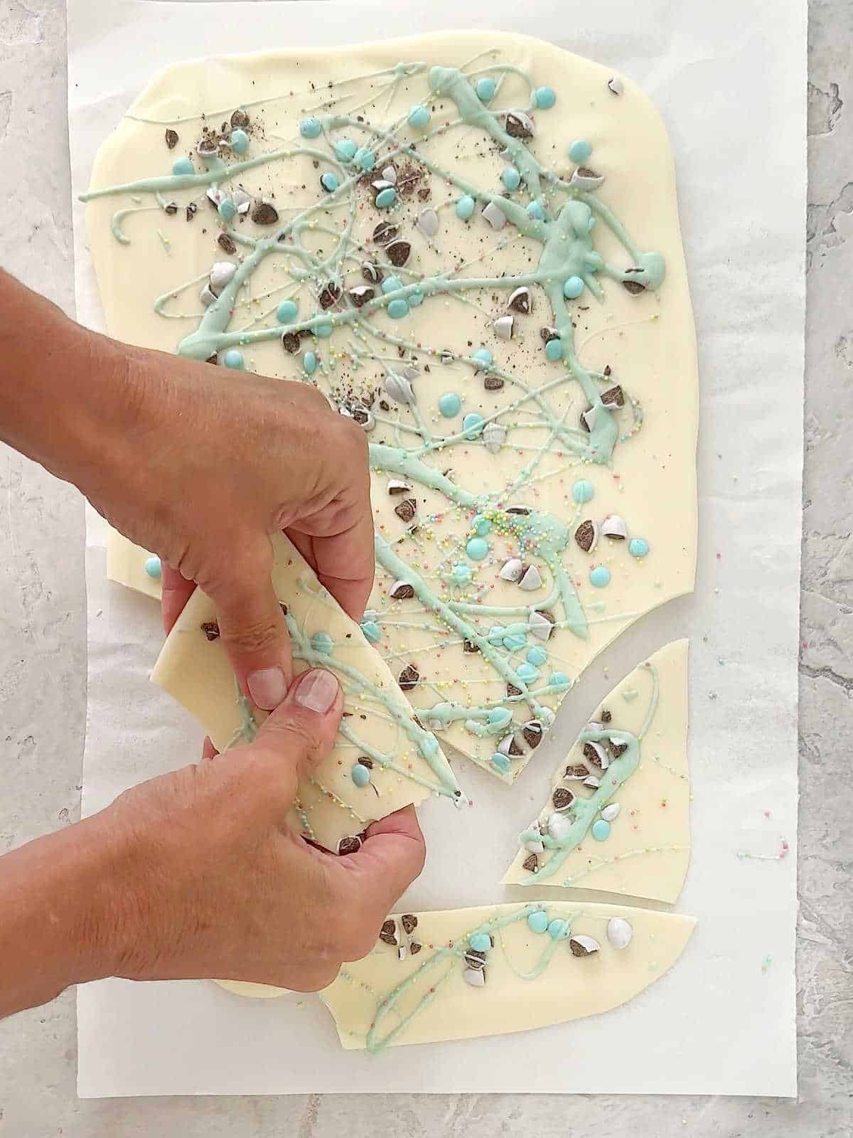 Breaking pieces of white and pastel green chocolate bark on parchment paper. View from above.