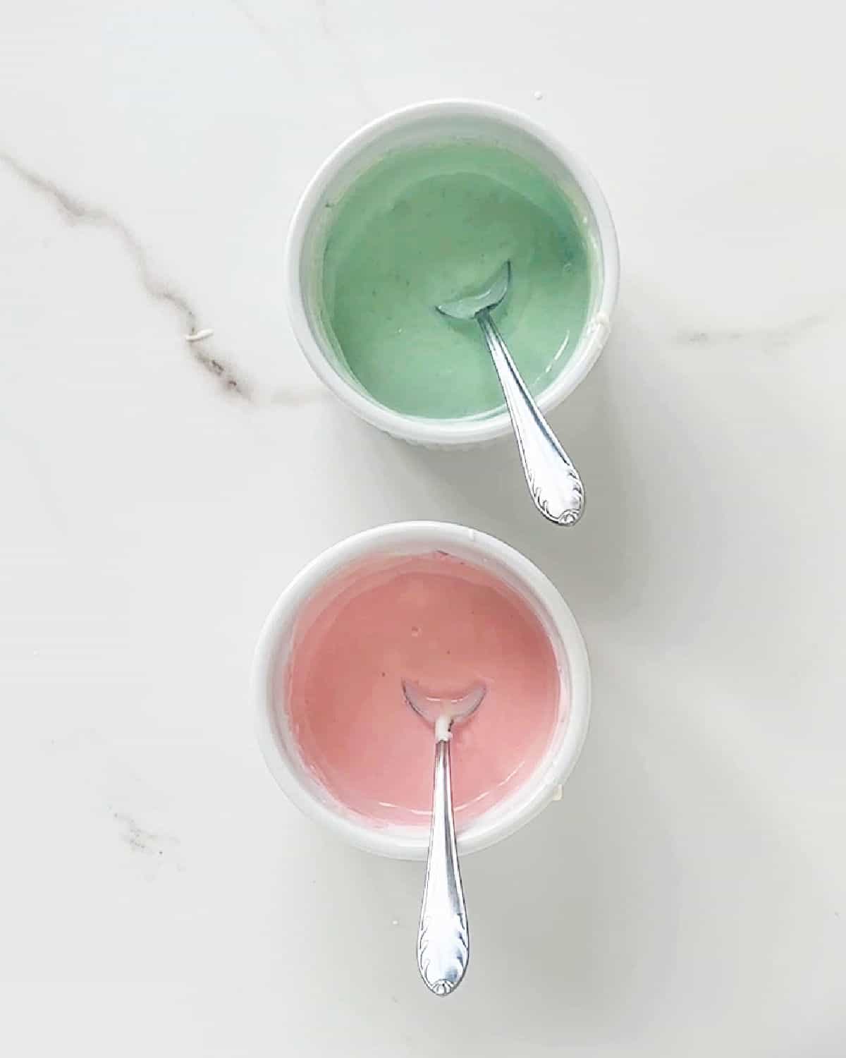 White bowls on white marble with pastel colored chocolate. Silver spoons inside.