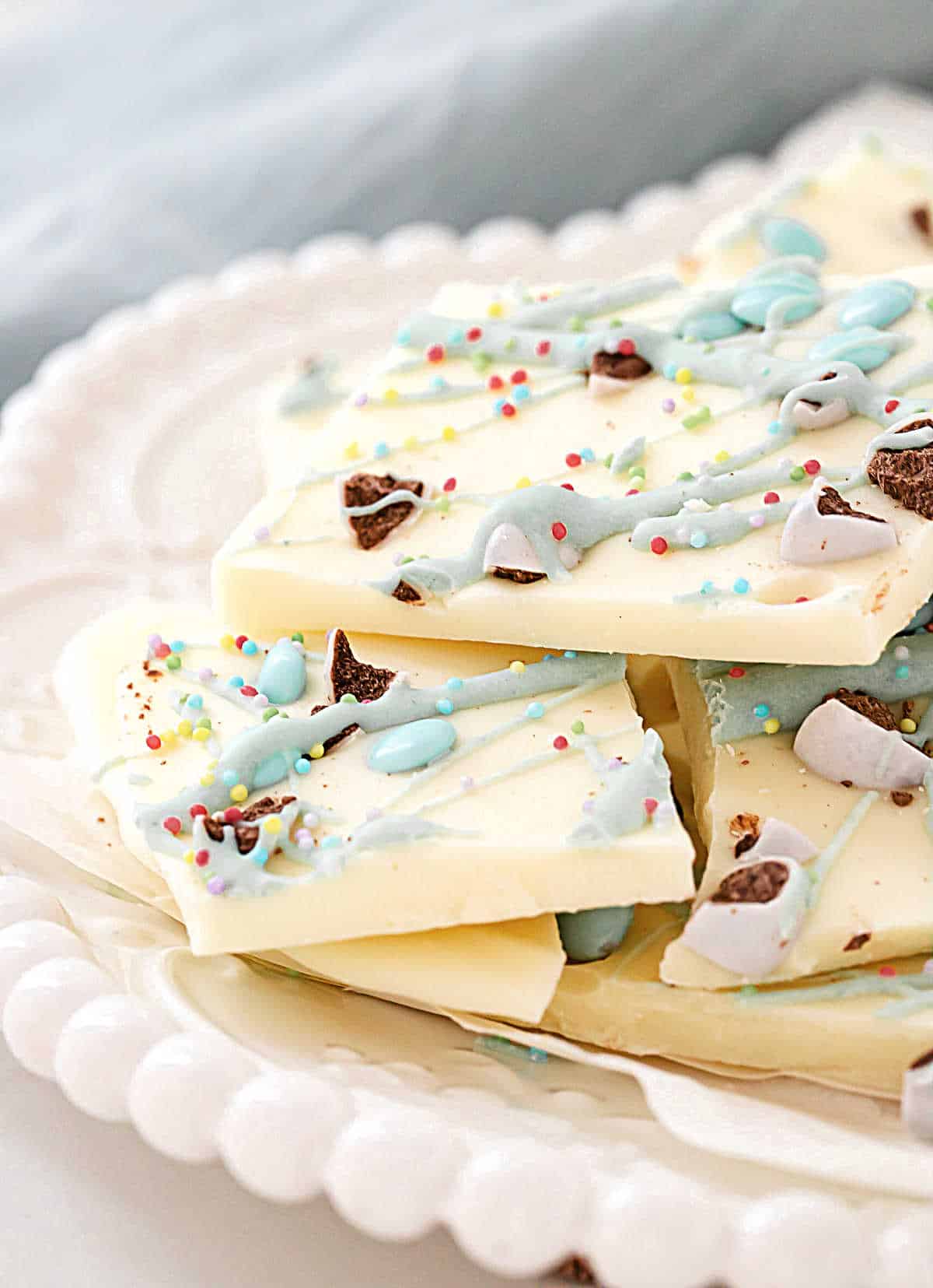 Close up of white chocolate Easter bark pieces on a white plate. Light blue cloth in the background. 