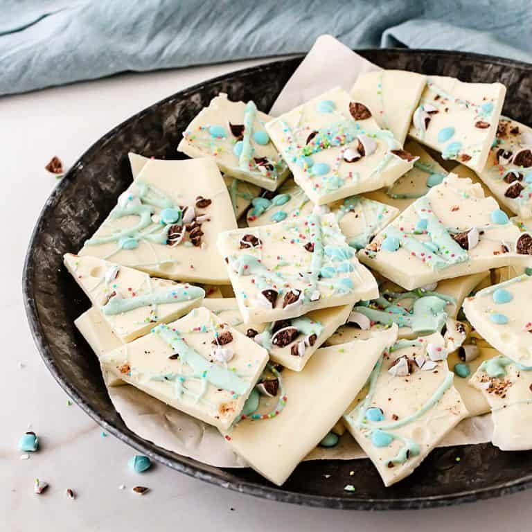 Metal plate with pieces of white and pastel chocolate Easter bark. White surface and blue cloth in the background.
