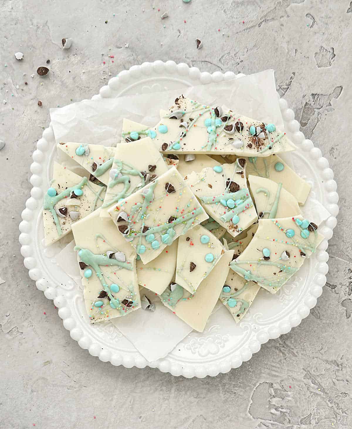 Overview of white chocolate Easter bark pieces on a white plate on a grey surface.