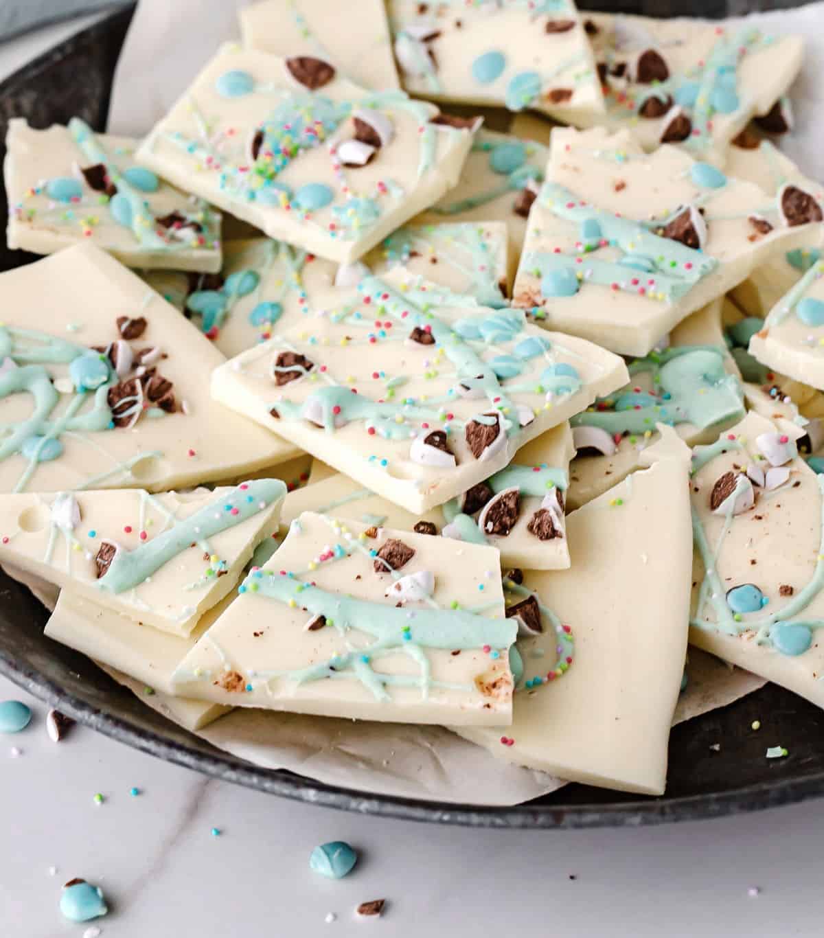 Overview of white chocolate Easter bark pieces on a white plate on a grey surface.