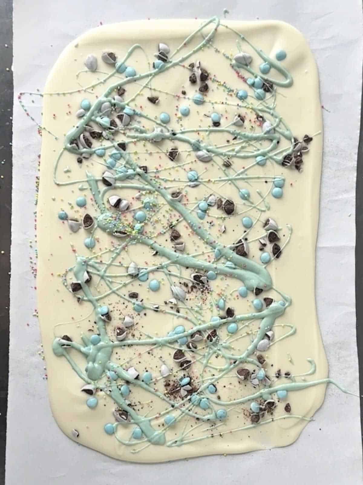 White chocolate Easter bark with chopped mini eggs, sprinkles and pastel green drizzles on a white paper.