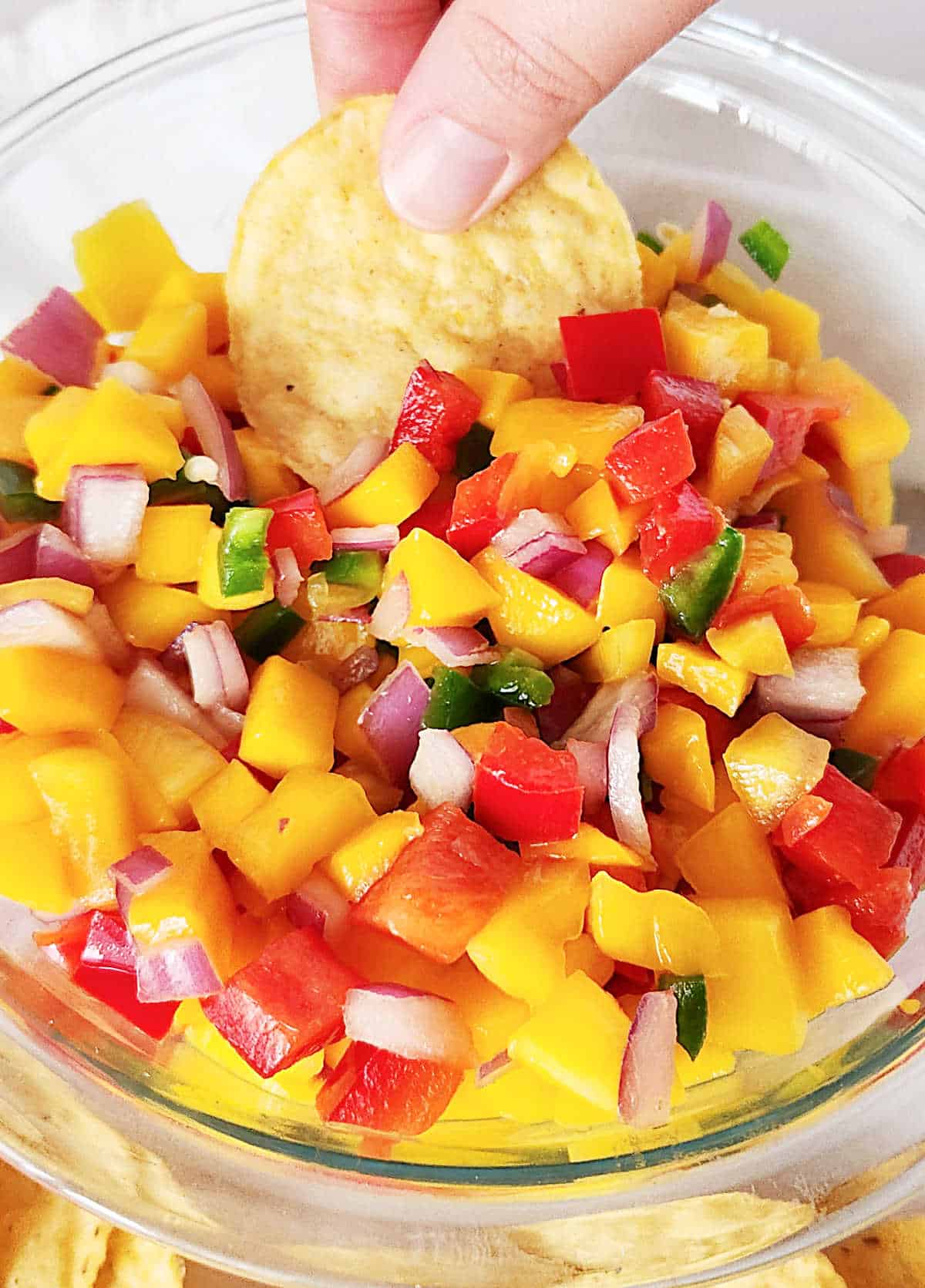 Close up of mango peach salsa in a glass bowl with hand holding a corn chip.