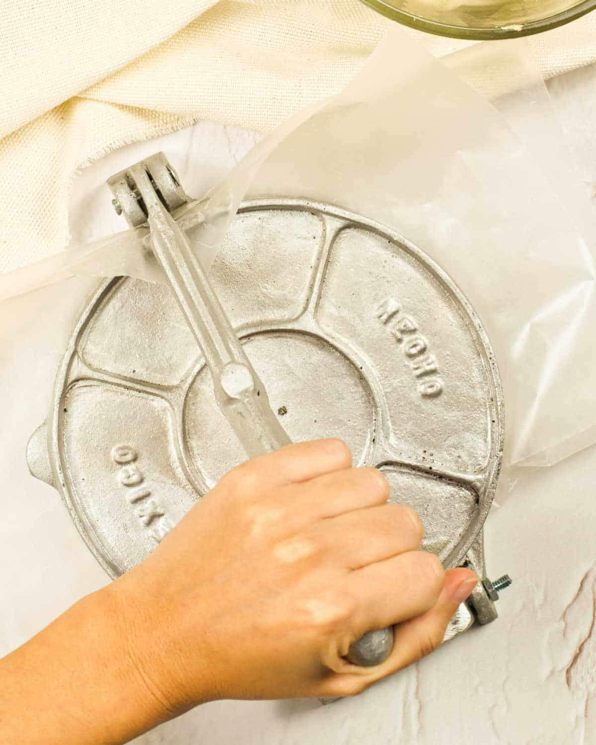 A hand closing a tortilla press on a white surface.