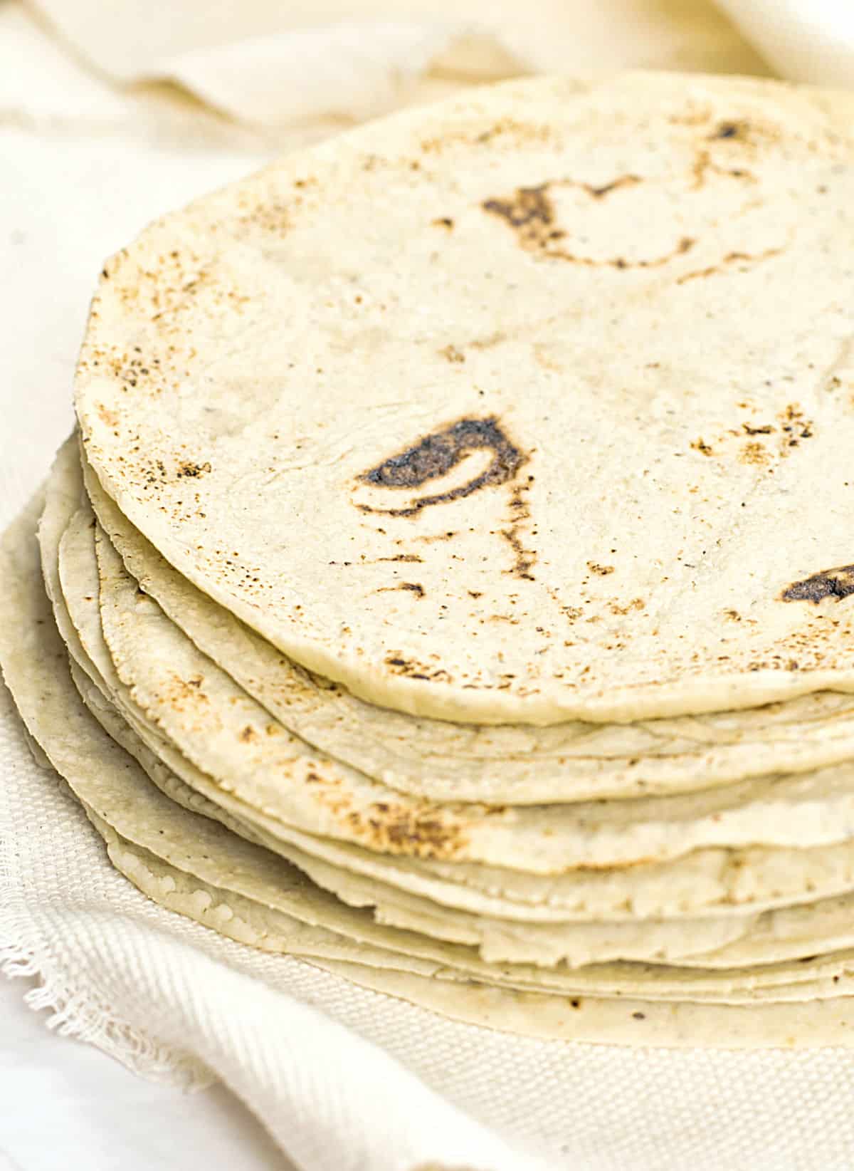 Stacked homemade corn tortilla on a cream colored cloth. 