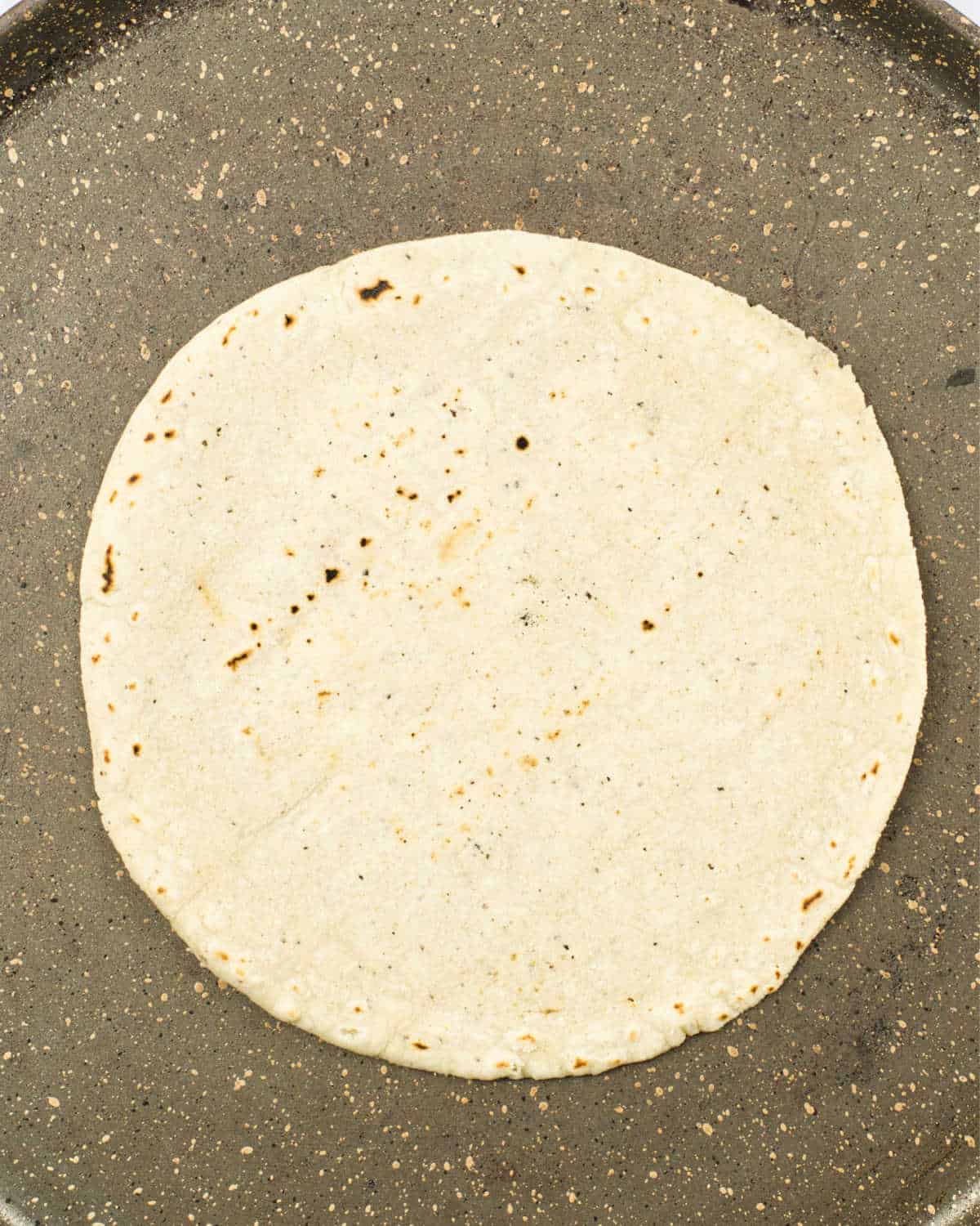 Dark griddle with corn tortilla cooking. Top close up view.