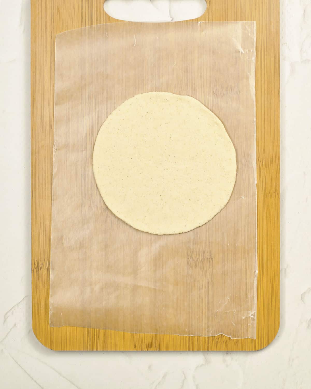 Rolled corn tortilla on wax paper set on a wooden board. Light grey surface. 