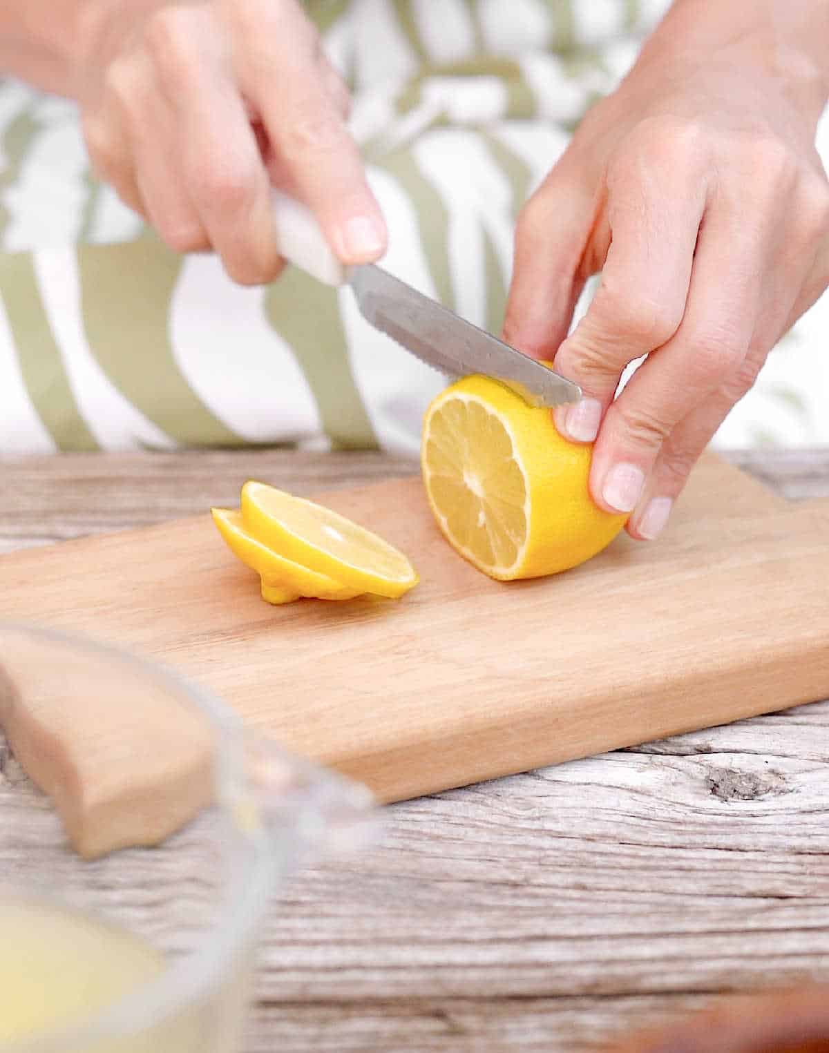 Person with green and white dress cutting lemon slices on a light colored wooden board.
