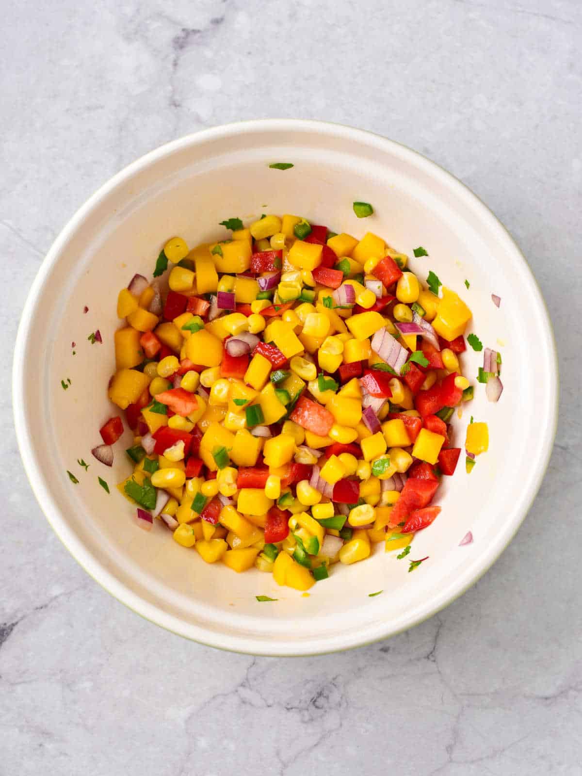 White bowl with mixed mango corn salsa. Grey marble surface.