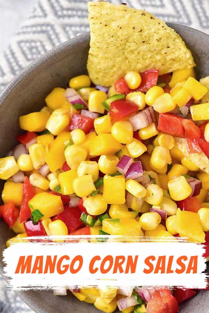 Orange and white text overlay on image of corn mango salsa with chips in a grey bowl.