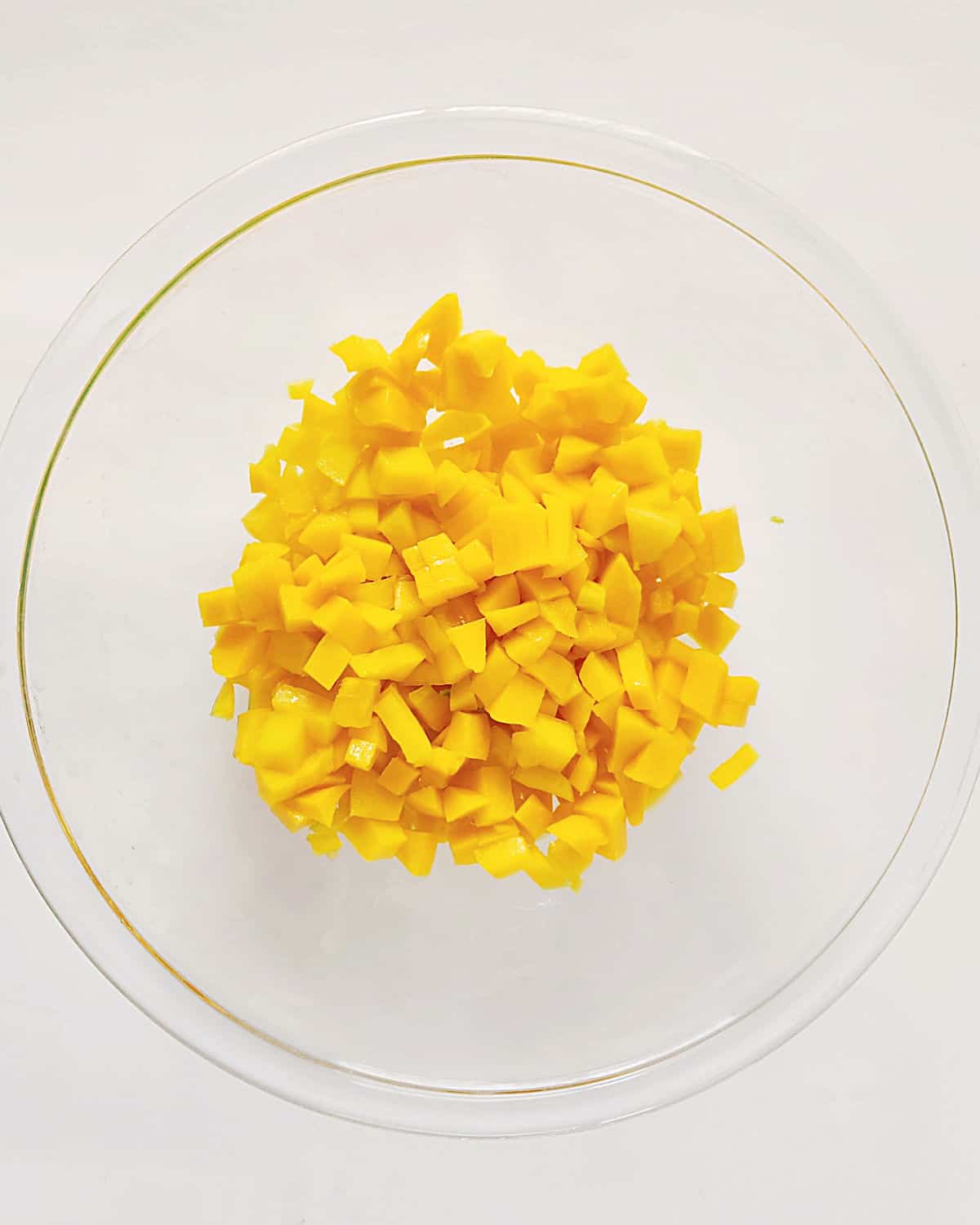 Chopped mango and peach in a glass bowl on a white surface.