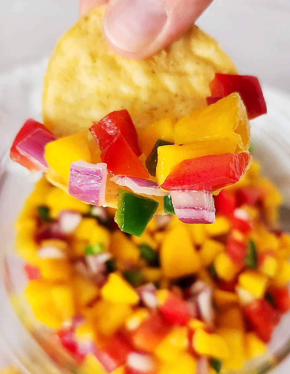 Corn chip with mango peach salsa held over bowl with more salsa.